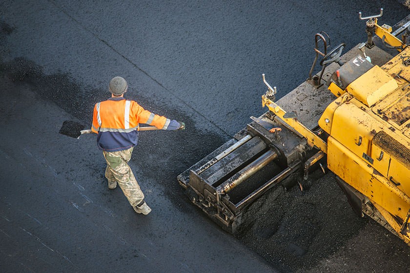 Eine Asphaltspur wird mit  Hilfe von einer Maschine und einem Menschen gelegt